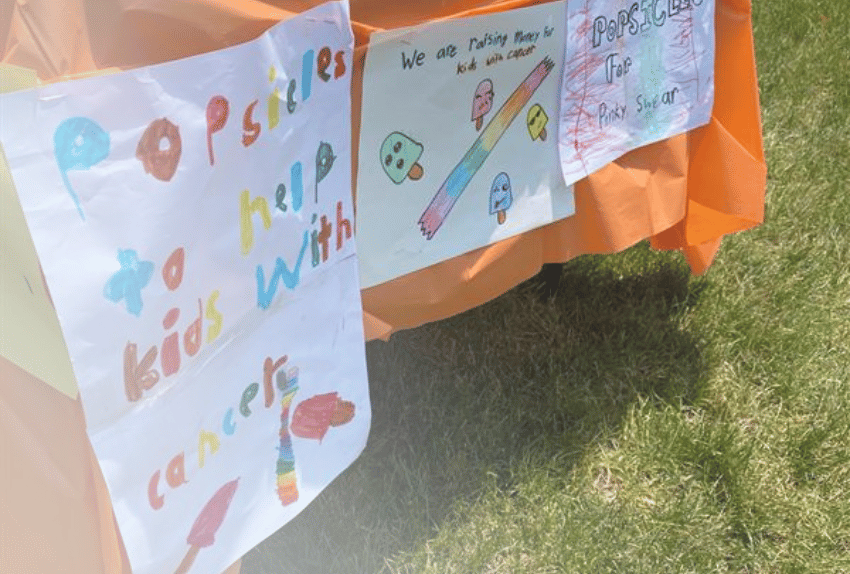 Signs hanging from a table advertising Popsicles for Pinky Swear in colorful kids marker writing