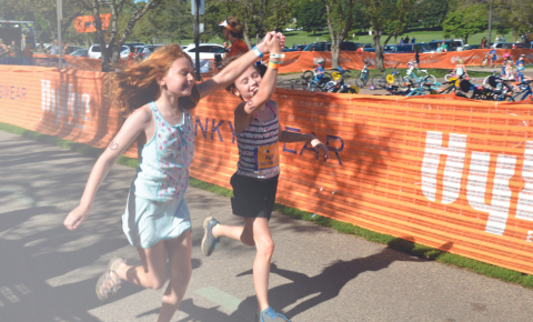 Two girls holding hands while coming through the finish line at a Hy-Vee Triathalon to support Pinky Swear Foundation