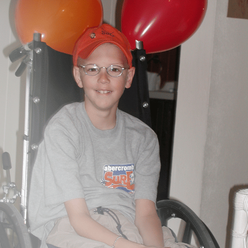 Pinky Swear founder and All-Star Mitch sitting in a wheelchair with an orange and red balloon tied to it.